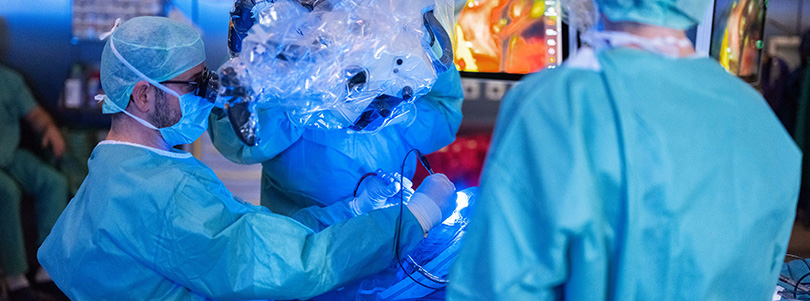 Fluoreszenzgestützte neurochirurgische Operation Neurochirurgisches Operationsteam bei einem Eingriff unter dem Operationsmikroskop